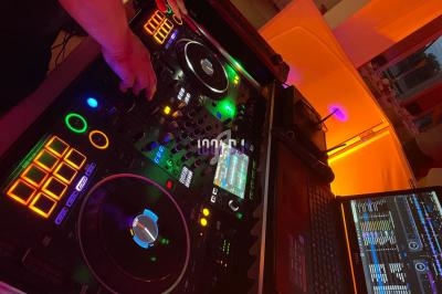 Console de mixage DJ avec platines, boutons lumineux et ordinateur portable affichant des pistes audio.