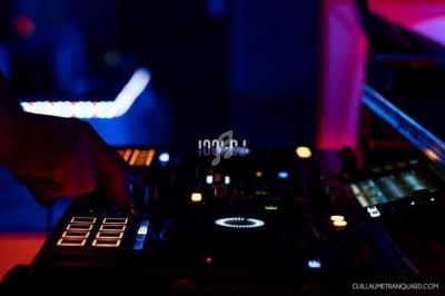 Main posée sur une table de mixage éclairée dans une ambiance sombre avec des lumières colorées.