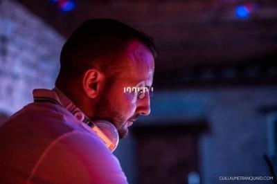 Homme portant un casque audio, concentré dans un environnement faiblement éclairé avec des lumières colorées.