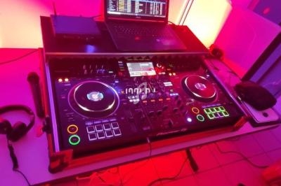 Console de mixage DJ avec platines, casque et ordinateur portable, éclairée par des lumières rouges et violettes.