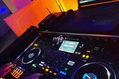 Poste de DJ avec platines lumineuses, ordinateur portable affichant un logiciel de mixage et ambiance colorée en arrière…