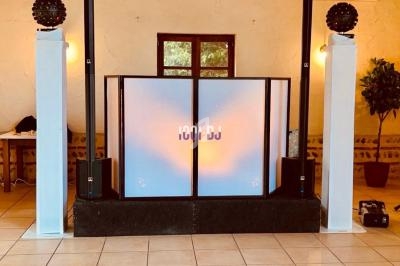 Configuration d'une cabine DJ avec éclairage coloré, deux colonnes lumineuses et des enceintes dans une salle intérieure.