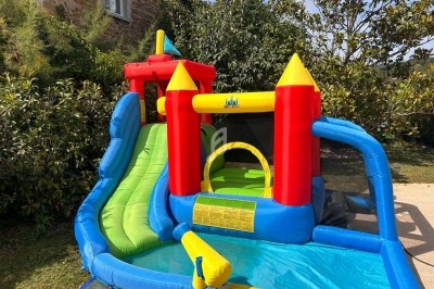 Château gonflable coloré avec toboggan et piscine intégré, installé dans un jardin ensoleillé.
