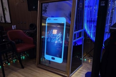 Miroir interactif lumineux en forme de smartphone utilisé comme borne photo dans un espace intérieur décoré.
