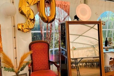 Fauteuil rouge, miroir doré et ballons ’50’ dans une tente décorée pour une célébration.