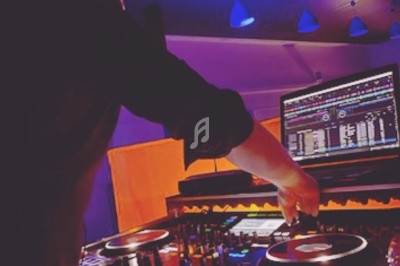 Un DJ mixant de la musique sur une table de mixage éclairée, avec un écran affichant des pistes audio.