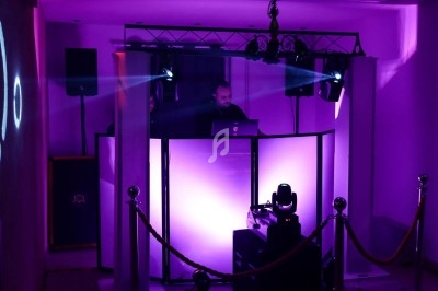 Un DJ mixe derrière une table éclairée de lumières violettes dans une salle sombre avec des équipements audio.