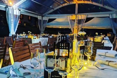 Salle de réception sous une verrière éclairée, avec tables dressées, nappes blanches et décorations lumineuses.