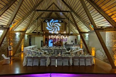 Salle de réception en bois avec tables dressées, éclairage chaleureux et espace DJ en fond.