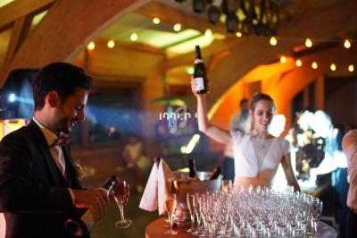 Un couple sert du champagne lors d'une réception festive dans une salle éclairée et décorée.