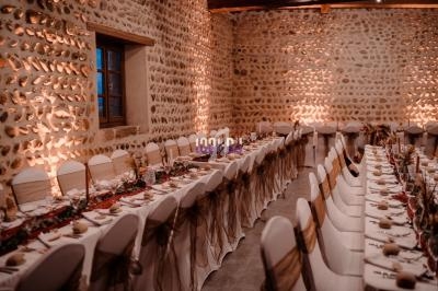 Salle de réception en pierre avec tables décorées, alignées et dressées pour un événement festif.