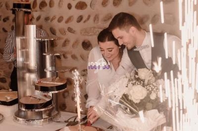 Un couple coupe un gâteau de mariage sur une table décorée, avec des étincelles et des fleurs blanches en arrière-plan.