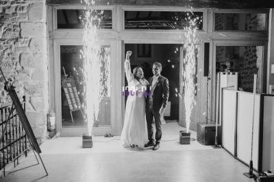 Un couple souriant célèbre devant des étincelles dans une salle avec murs en pierre et grandes baies vitrées.