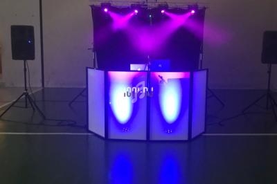 Poste de DJ avec éclairage violet et bleu, deux haut-parleurs sur trépieds, installé dans une salle sombre.