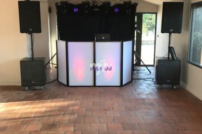 Installation de matériel de DJ avec une table lumineuse, des enceintes et des jeux de lumière dans une salle au sol en terre…