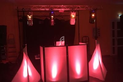 Installation de DJ avec une table éclairée en rouge, des spots lumineux suspendus et un fond sombre.