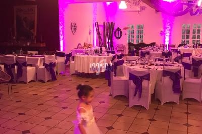 Une salle de réception décorée en violet avec des tables dressées et une enfant en robe blanche au premier plan.