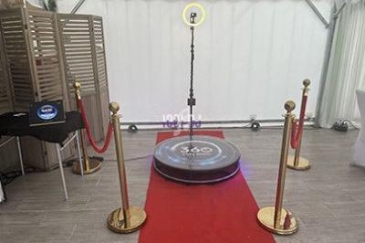 Plateforme circulaire de vidéobooth 360 entourée de poteaux dorés et d'un tapis rouge dans un espace intérieur.