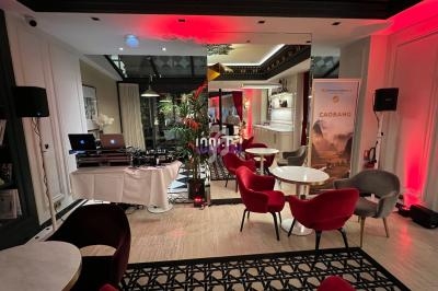 Salle élégante avec tables, chaises rouges, plantes, éclairage tamisé et équipement de DJ installé près d'un miroir.