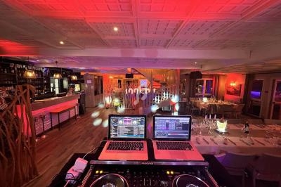 Vue d'une salle de réception éclairée avec des lumières colorées, tables dressées et équipement de DJ au premier plan.