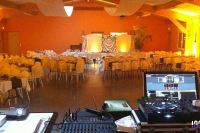 Salle de réception décorée avec des tables dressées, vue depuis une table de mixage de DJ au premier plan.