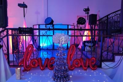 Décoration de fête avec ballons rouges ’love’, tour de bonbons, guirlandes lumineuses et éclairage coloré en arrière-plan.