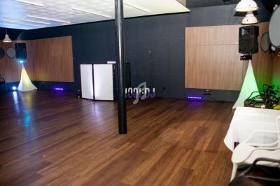 Salle vide avec parquet, éclairages colorés, enceintes murales et une table équipée dans un coin.