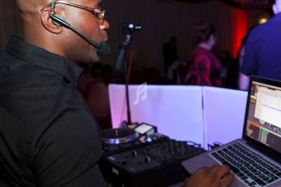 Un DJ mixe de la musique sur un ordinateur portable et une table de mixage dans une salle éclairée.