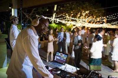 Un DJ mixe de la musique lors d'une soirée en plein air, avec des invités dansant sous des guirlandes lumineuses.