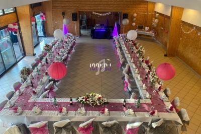 Salle décorée pour une réception, avec deux longues tables en U ornées de nappes roses, lanternes et fleurs.