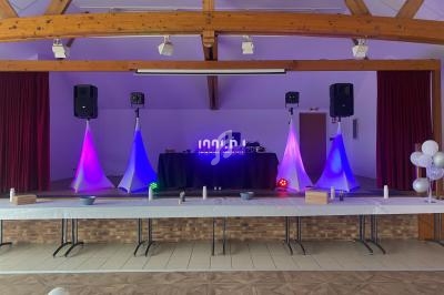 Salle décorée pour un événement avec une table dressée au premier plan et une scène équipée de lumières colorées.
