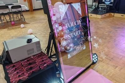 Miroir interactif avec cadre lumineux rose, installé sur un parquet, entouré de ballons et d'équipements de fête.