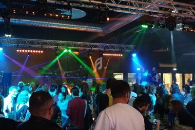 Groupe de personnes dans une salle de concert ou discothèque, éclairée par des lumières colorées et des projecteurs.