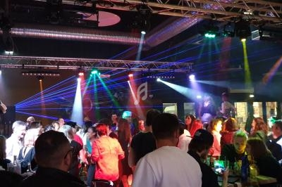 Groupe de personnes dans une salle de fête avec jeux de lumières colorées et ambiance animée.