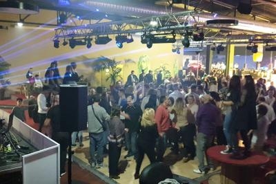 Salle animée avec une foule dansante, éclairée par des jeux de lumières colorés, et un DJ en arrière-plan.