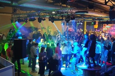 Personnes dansant et socialisant sur une piste de danse éclairée par des lumières colorées dans un espace intérieur animé.