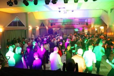 Salle comble avec des personnes dansant sous des lumières colorées lors d'un événement festif en intérieur.