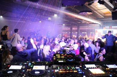 Vue d'une piste de danse bondée dans une ambiance festive, avec une table de mixage au premier plan.
