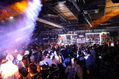Foule dans une discothèque animée avec éclairages colorés, bar en arrière-plan et ambiance festive.