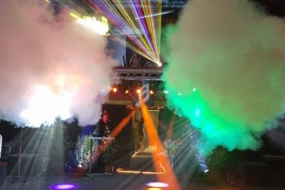 Effets lumineux colorés et fumée dans une salle sombre, avec des éléments de décor et des lits visibles.