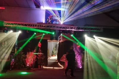 Salle sombre décorée avec des lumières colorées, des lasers et des éléments végétaux, ambiance festive.