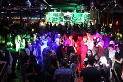 Personnes dansant et socialisant dans une salle de fête éclairée par des lumières colorées et décorée de guirlandes.