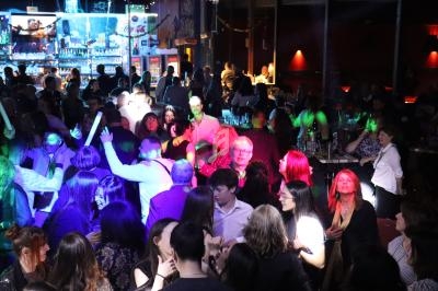 Groupe de personnes dans une ambiance festive avec éclairages colorés, dans un bar ou une salle animée.