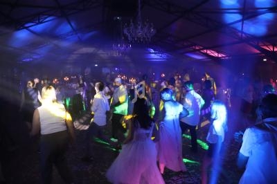 Des personnes dansent sous des jeux de lumière colorés dans une grande salle avec un plafond métallique et des chandeliers.