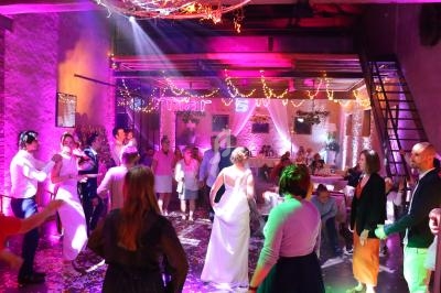 Des invités dansent sous des lumières colorées lors d'une fête dans une salle décorée avec guirlandes lumineuses.