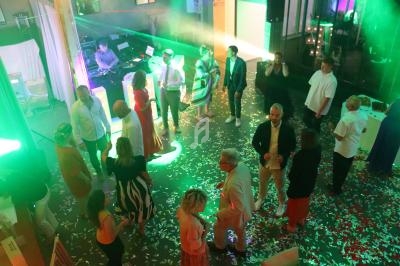 Personnes dansant et discutant sur une piste éclairée par des lumières colorées, avec un DJ en arrière-plan.