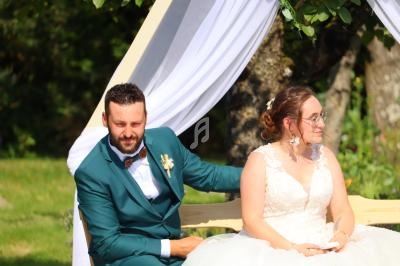 Un couple assis sous une arche décorée de voilages blancs dans un jardin verdoyant.