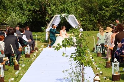 Un couple assis sous une arche décorée lors d'une cérémonie de mariage en plein air, entouré d'invités.