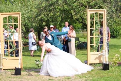 Un couple de mariés pose joyeusement dans un jardin, entouré d'invités et de décorations champêtres.