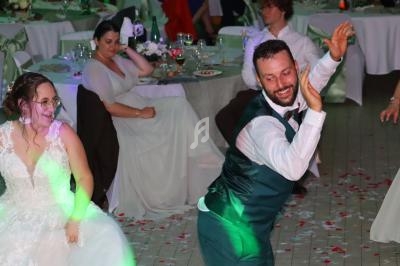 Un homme en costume danse avec énergie lors d'une réception de mariage, entouré d'invités assis à des tables décorées.